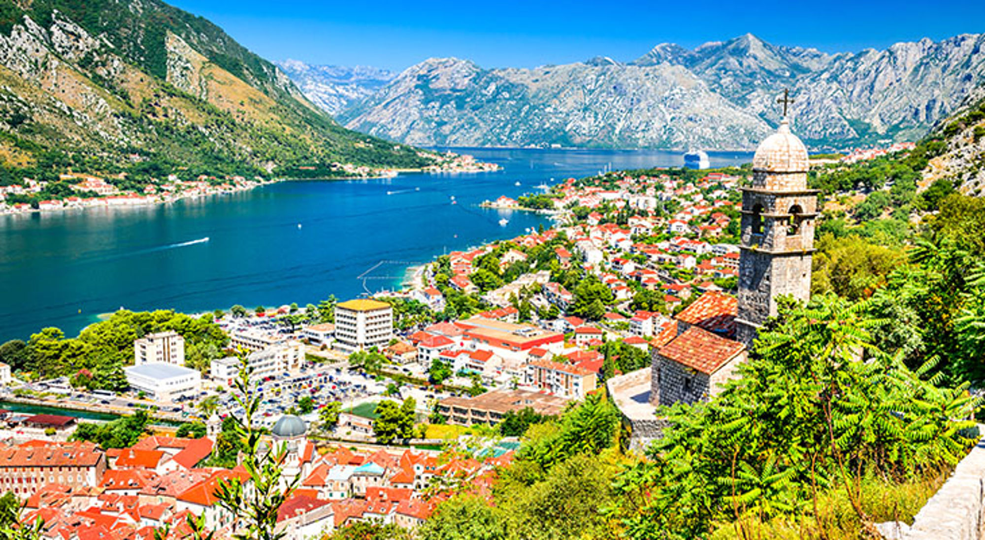 Single reis Montenegro Uitzicht over de Baai van Kotor met oude stad en kerktoren, omringd door bergen.