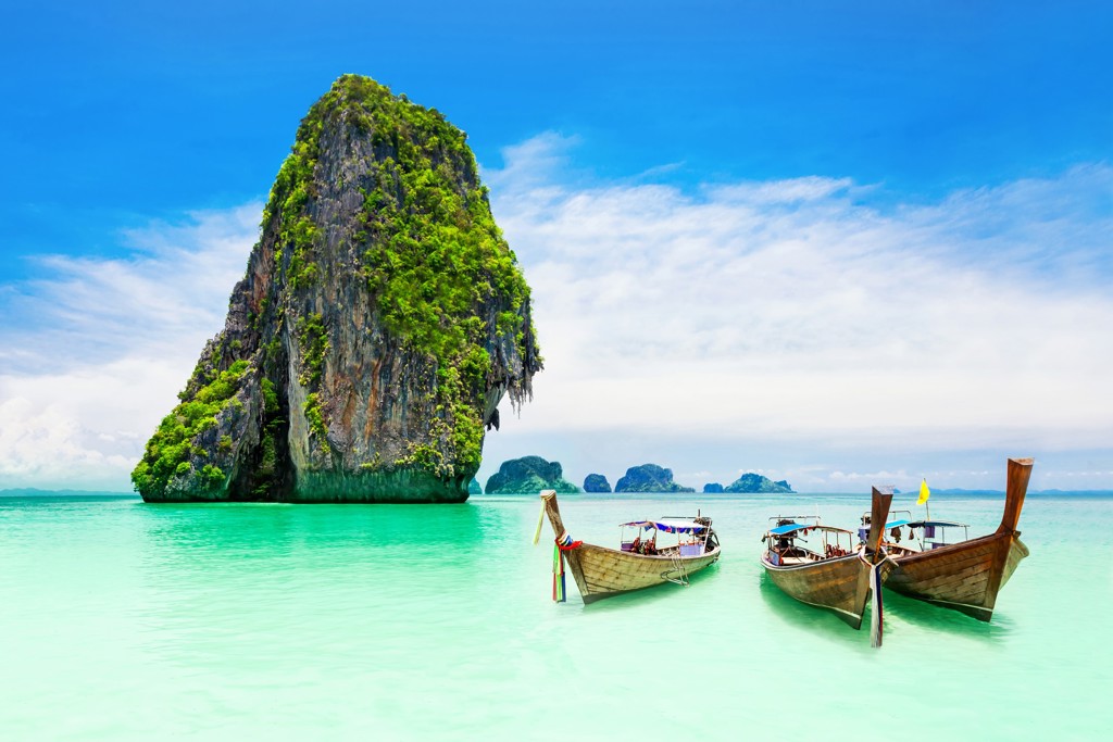 Longtailboten bij een kalkstenen rots in turquoise zee in Thailand.