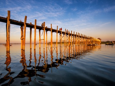 U Bein-brug bij Mandalay in Myanmar bij zonsondergang, met houten palen en weerspiegeling in het water.