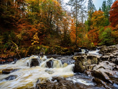 Herfstkleuren langs een snelstromende rivier met rotsen in de Schotse Hooglanden tijdens de Route Schotland.