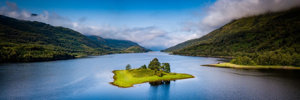 Groen eilandje in een Schots loch, omringd door bergen, tijdens een groepsrondreis in het Verenigd Koninkrijk.