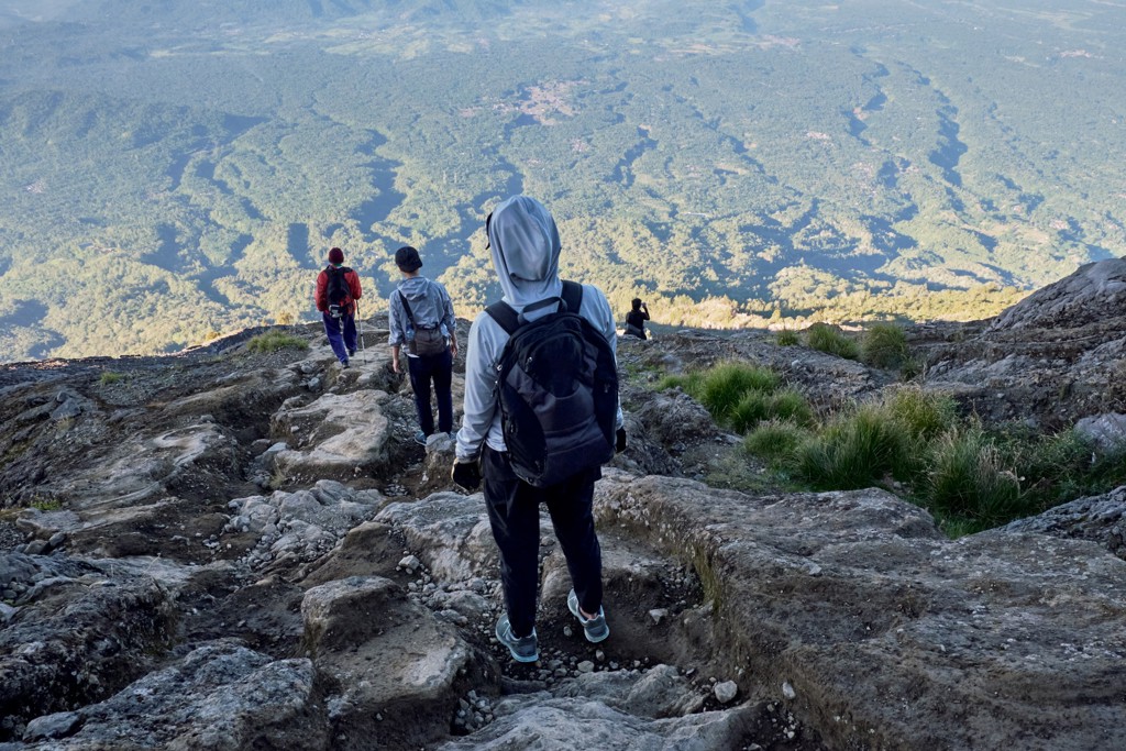 Wandelaars dalen af over rotsachtig bergpad met uitzicht op groene valleien tijdens familiereis Bali en Sulawesi.