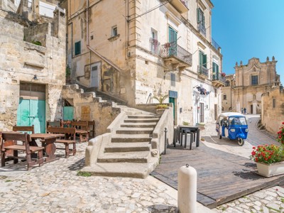 Straatbeeld in Matera met stenen trappen, historische gevels en een blauwe tuk-tuk in Puglia, Italië.