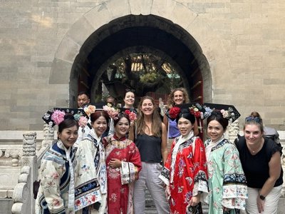 Groepsrondreis China: reizigers poseren met vrouwen in traditionele klederdracht bij een historische poort.