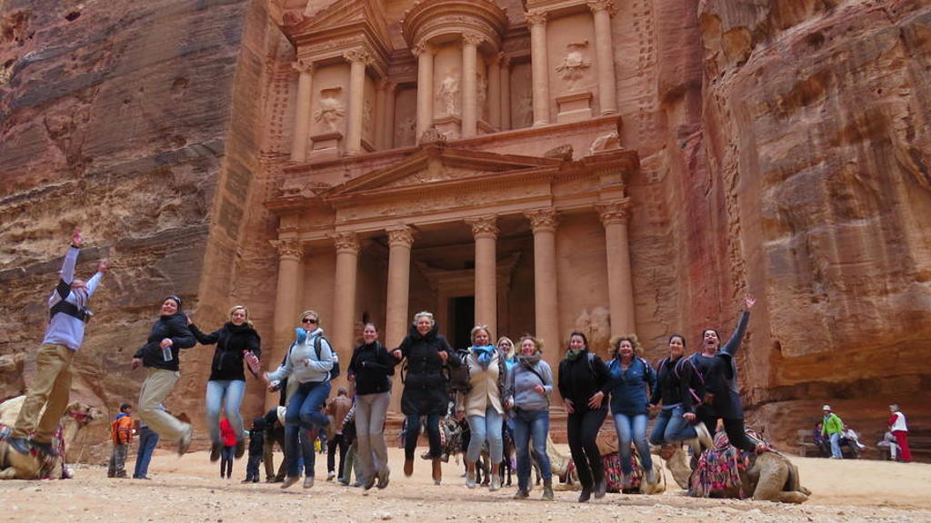 Groep reizigers springt voor de schatkamer Al-Khazneh in Petra, Jordanië.