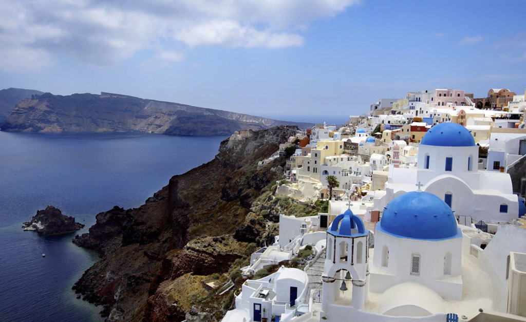 Witte huizen en blauwe koepelkerk in Oia op Santorini, met uitzicht over de caldera en de Egeïsche Zee.