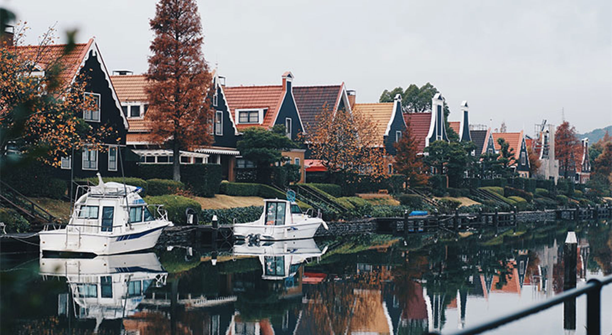 Themapark Huis ten Bosch Rivier met aangemeerde boten en huizen met puntgevels langs de oever, weerspiegeld in het water.