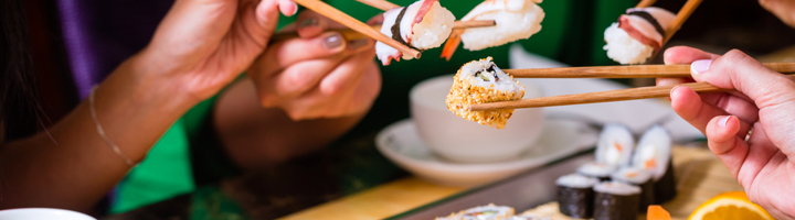 Mensen eten samen sushi met stokjes aan tafel.