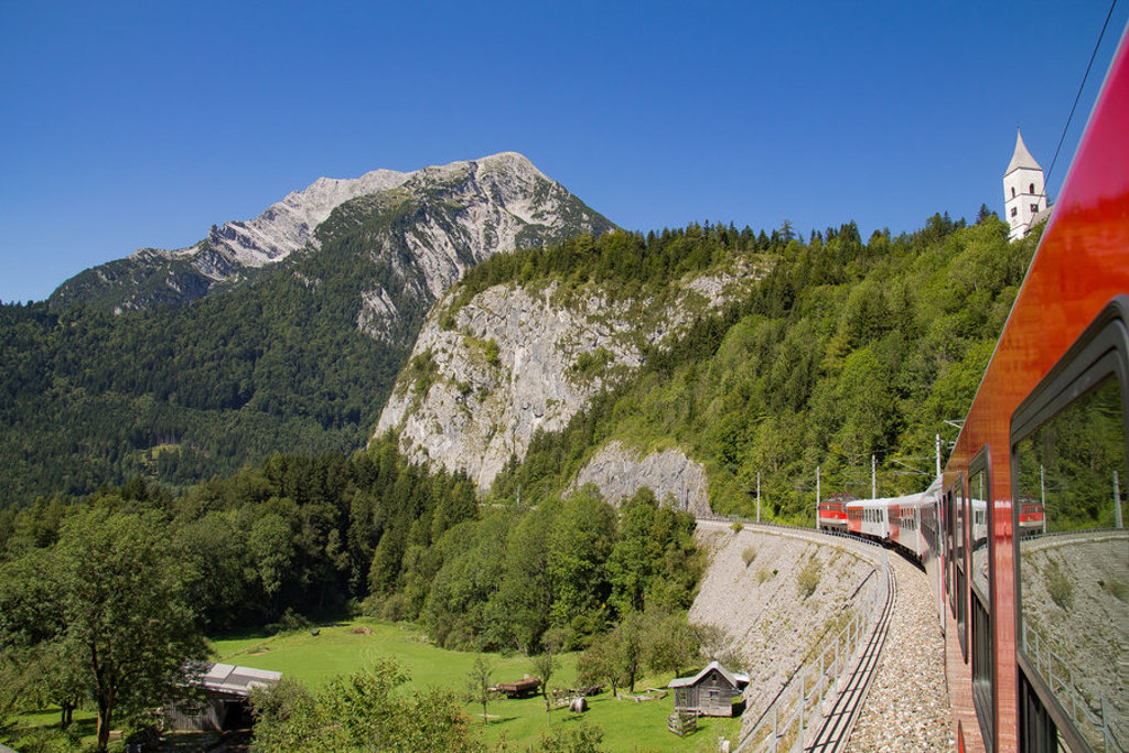 Treinreis door berglandschap in Centraal Europa, langs groene valleien en rotswanden onder een blauwe lucht.