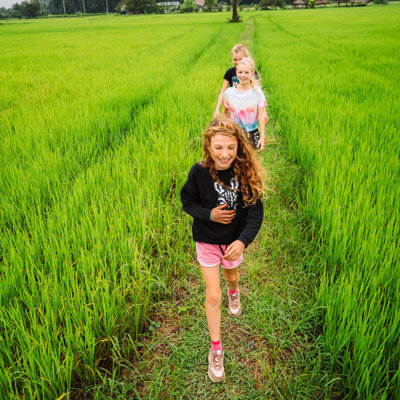 Kinderen wandelen over een pad door groene rijstvelden tijdens een familiereis in Thailand.