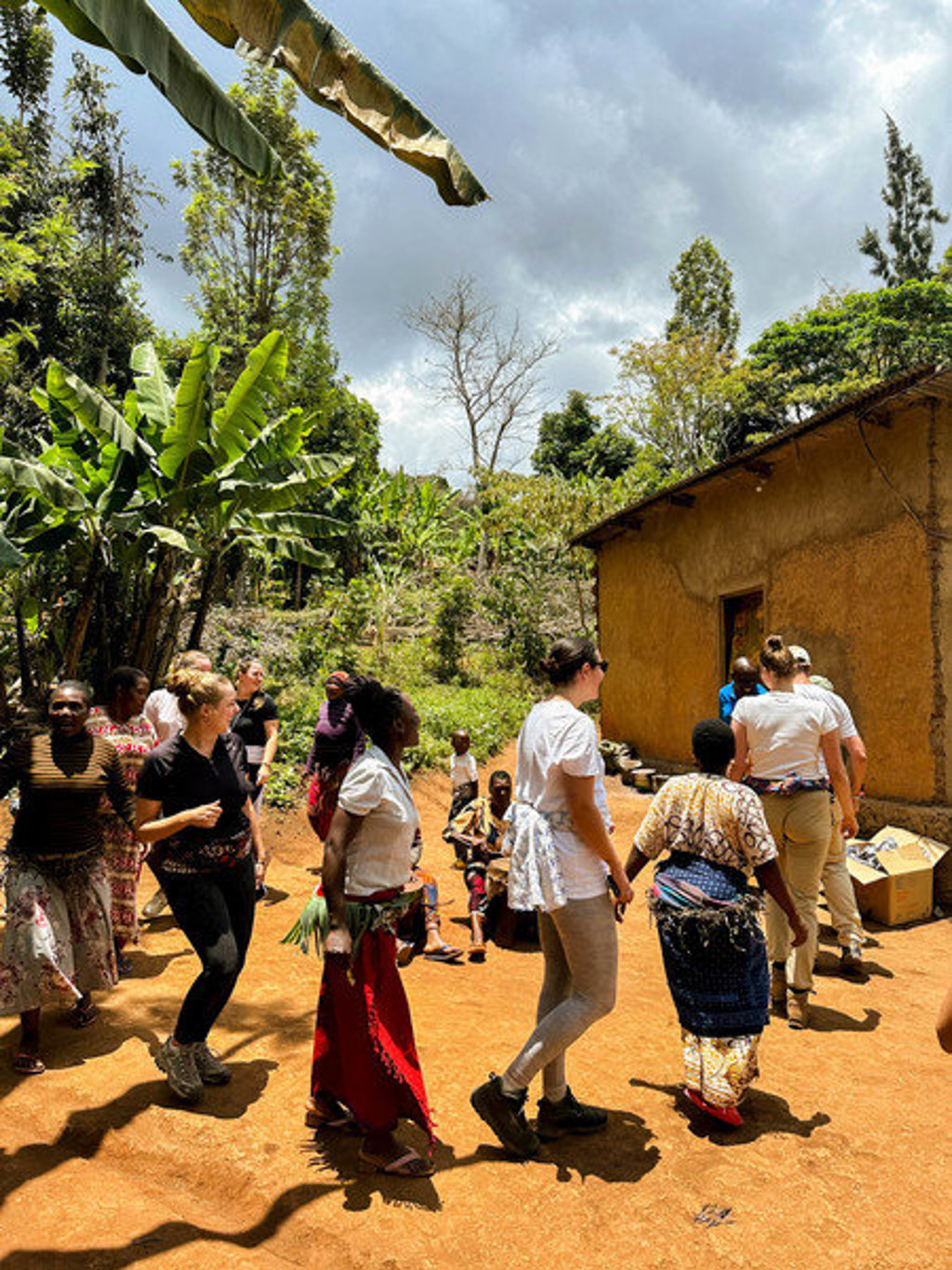 22-35ers reis Kenia & Tanzania: reizigers en locals dansen samen bij een huis in een groen dorp.