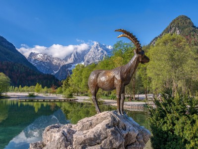 Bronzen steenbokbeeld bij een bergmeer met de Alpen op de achtergrond, Route Centraal Europa.