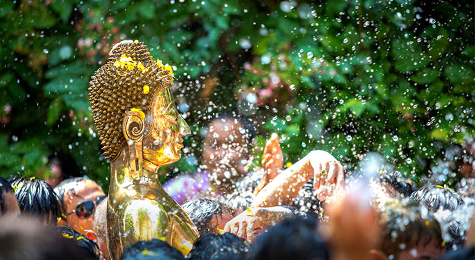 Boeddha beeld tijdens het Songkran Festival Gouden Boeddhabeeld tijdens het Songkran-waterfestival, omringd door feestvierders en opspattend water.