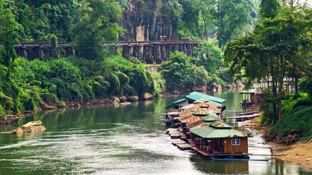 Drijvende bungalows op de River Kwai bij Kanchanaburi, Thailand, met groene jungle en houten spoorbrug.