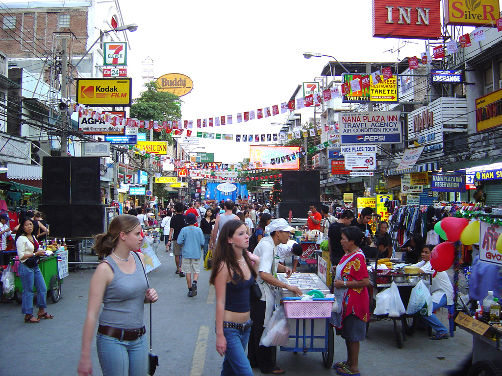 Drukke straatmarkt in Bangkok met kraampjes, reizigers en kleurrijke uithangborden tijdens een familiereis.