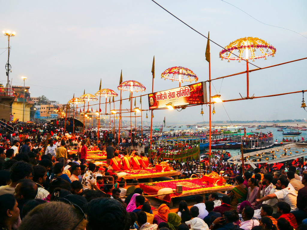 Drukke avondceremonie aan de Ganges in Varanasi, India, met verlichte parasols en boten op de rivier.