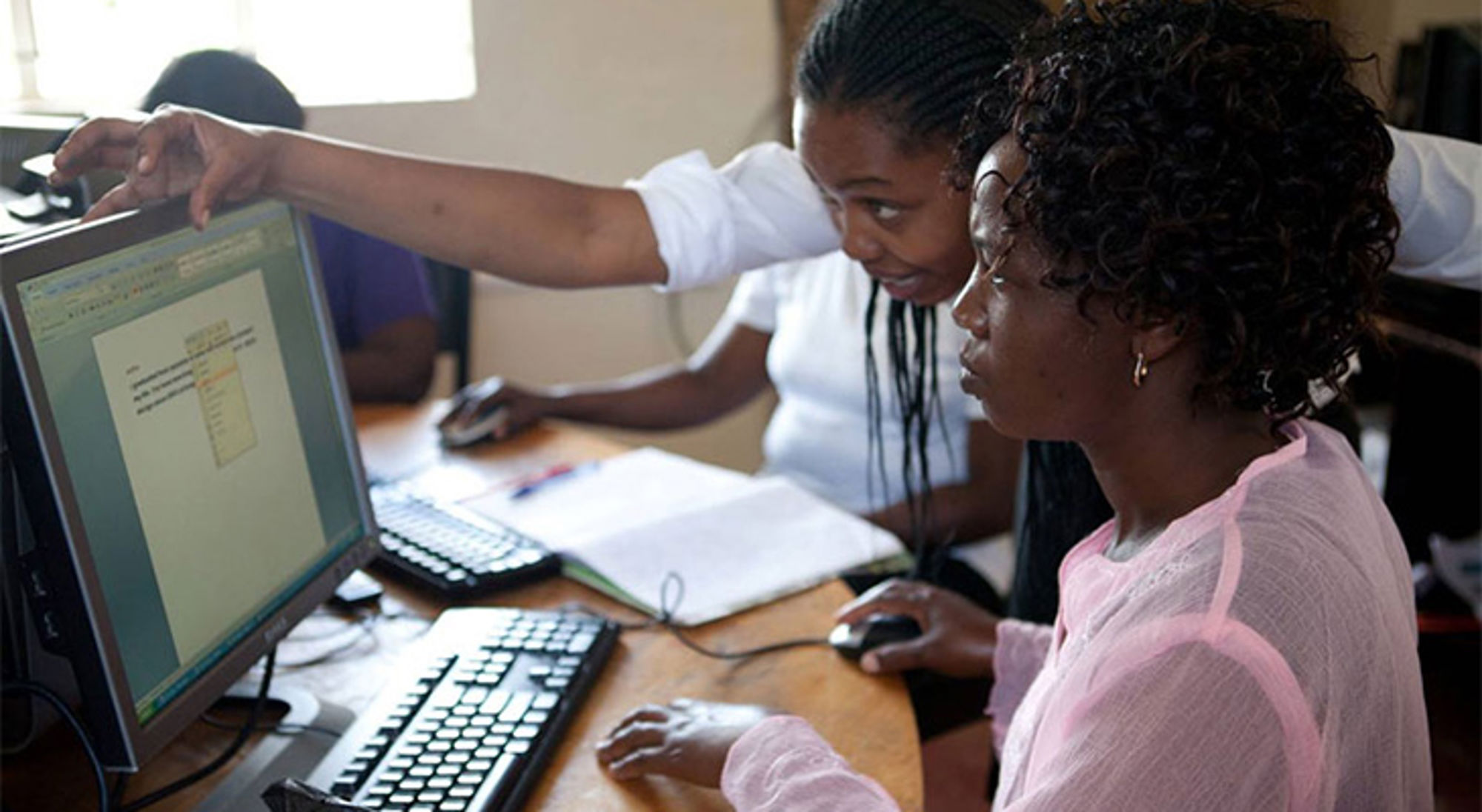 Stichting DEAN Twee vrouwen werken samen achter een computer en wijzen naar het scherm tijdens een les of training.