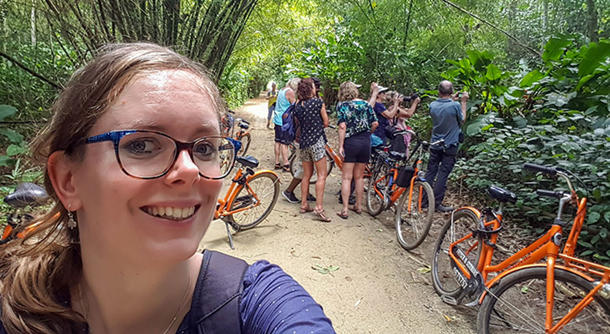 Selfie tijdens fietstocht met groep en oranje fietsen op een bospad tussen dicht groen.