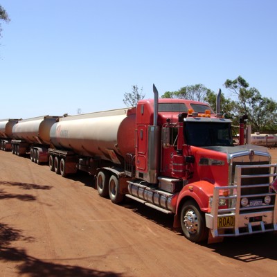 Rode road train met meerdere tanktrailers op een stoffige weg in de outback van Australië.