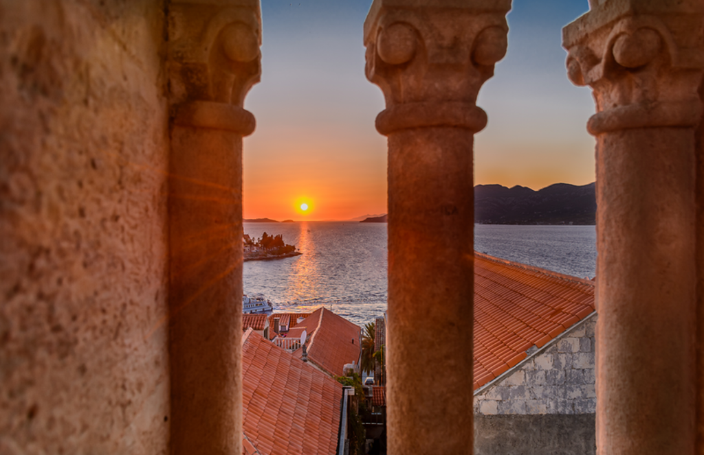 Zonsondergang over de Adriatische Zee, gezien tussen stenen zuilen boven de daken van Dubrovnik, Kroatië.