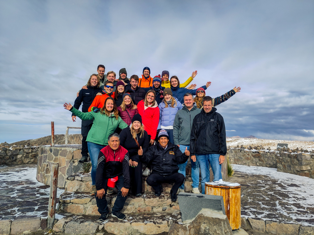 Groep 22-35ers op rondreis in Peru poseert in de Andes bij een besneeuwd uitkijkpunt.