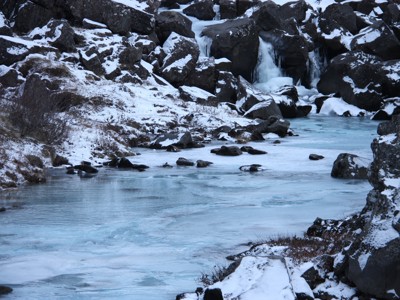 Bevroren rivier met kleine waterval tussen besneeuwde rotsen in IJsland tijdens de winterroute.