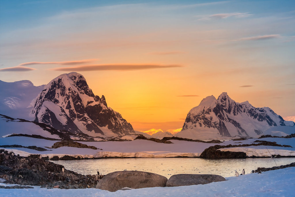 Zonsondergang boven besneeuwde bergen en zee-ijs in Antarctica tijdens een groepsrondreis per vliegtuig.