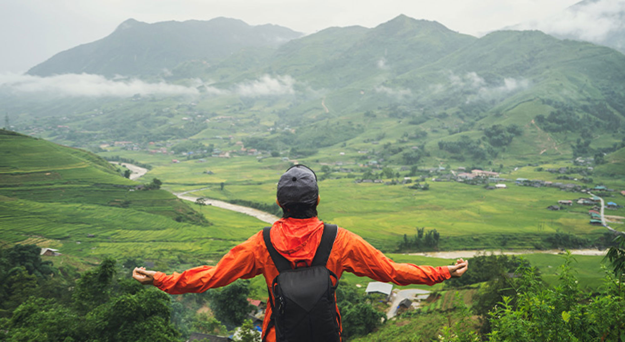 Regenseizoen Vietnam Wandelaar met rugzak kijkt uit over groene vallei met rivier en bergen in de mist.