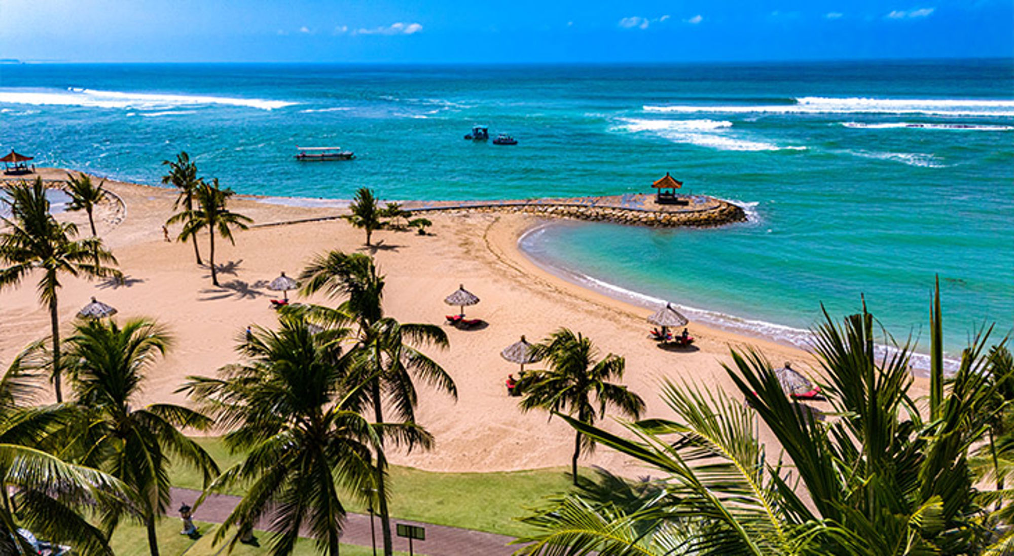 Nusa Dua Beach Bali Tropisch strand met palmbomen, rieten parasols en turquoise zee met golven.