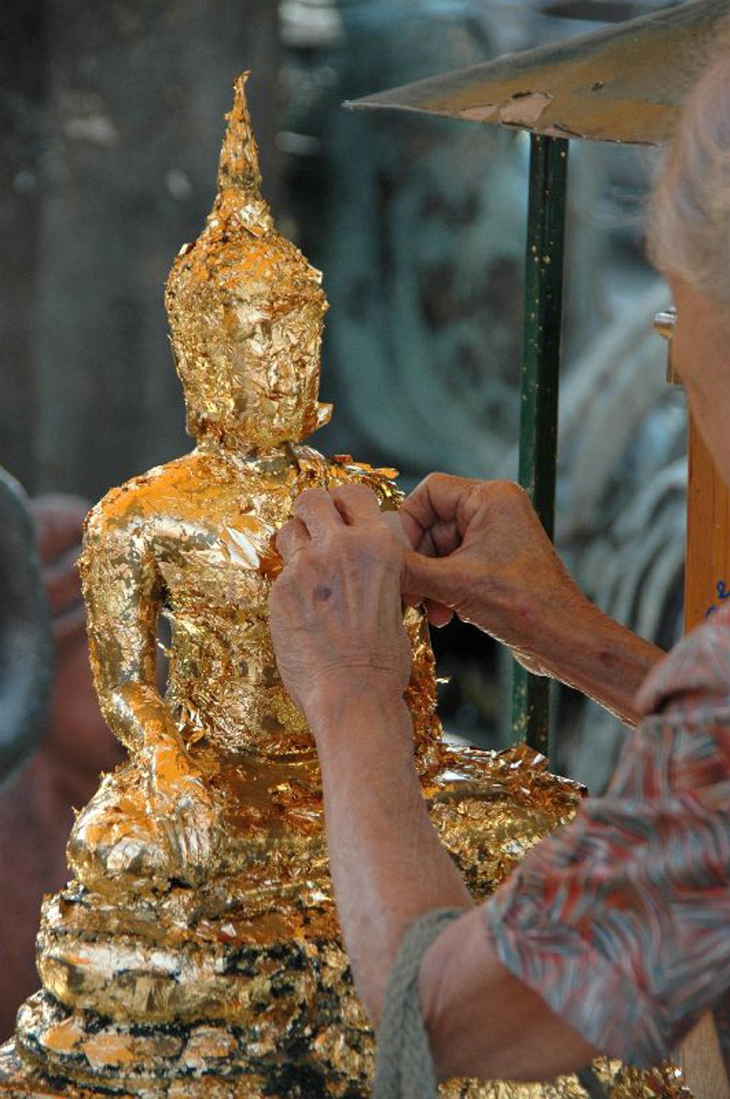 Goudblad aanbrengen op een Boeddhabeeld in een tempel tijdens de groepsrondreis Thailand Hoogtepunten.