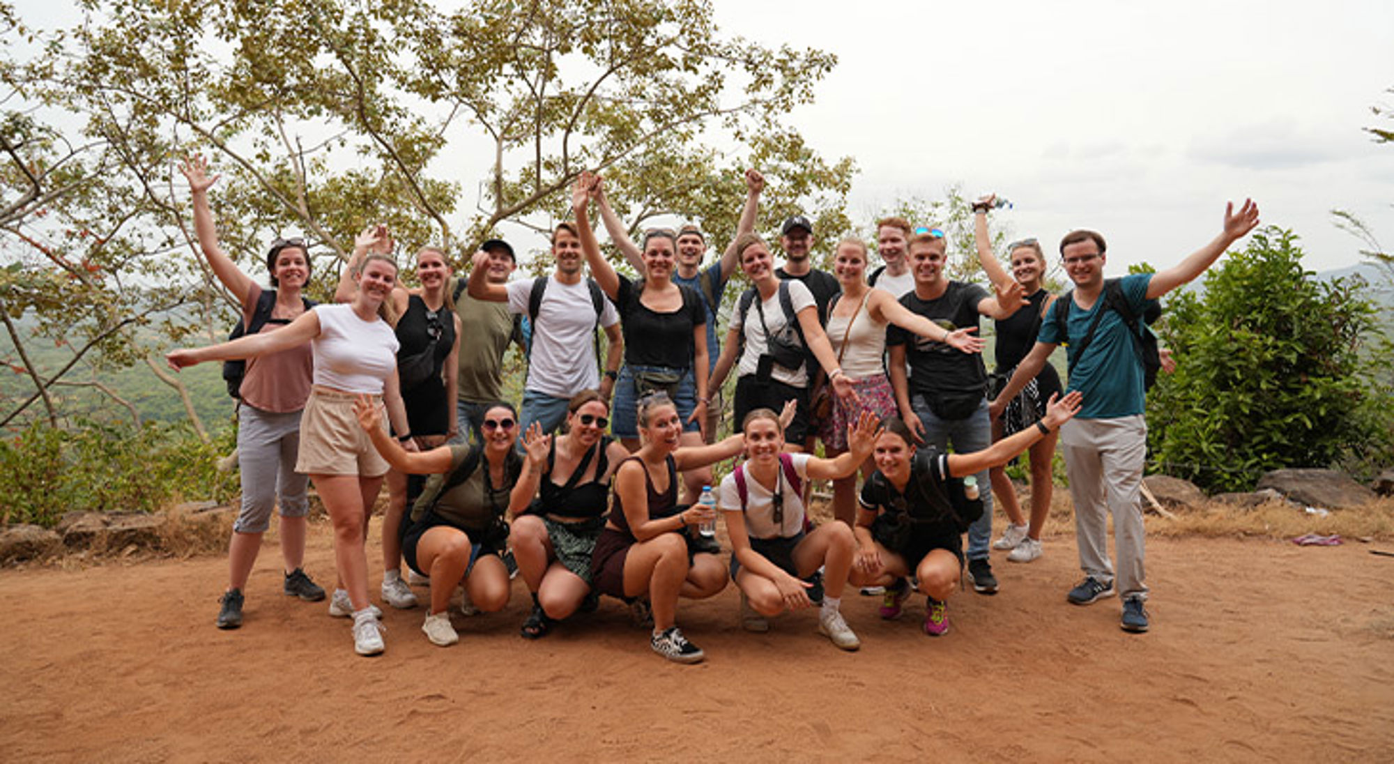 Groep reizigers poseert met opgeheven armen tijdens een hike op een uitkijkpunt in de natuur.
