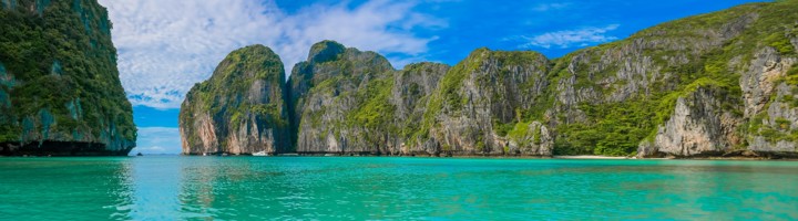 Maya Bay in Thailand met turquoise zee, wit zandstrand en steile kalksteenkliffen onder een blauwe lucht.