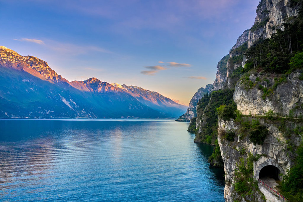 Uitzicht op het Gardameer met berglandschap en rotswand met tunnel bij zonsondergang in Italië.