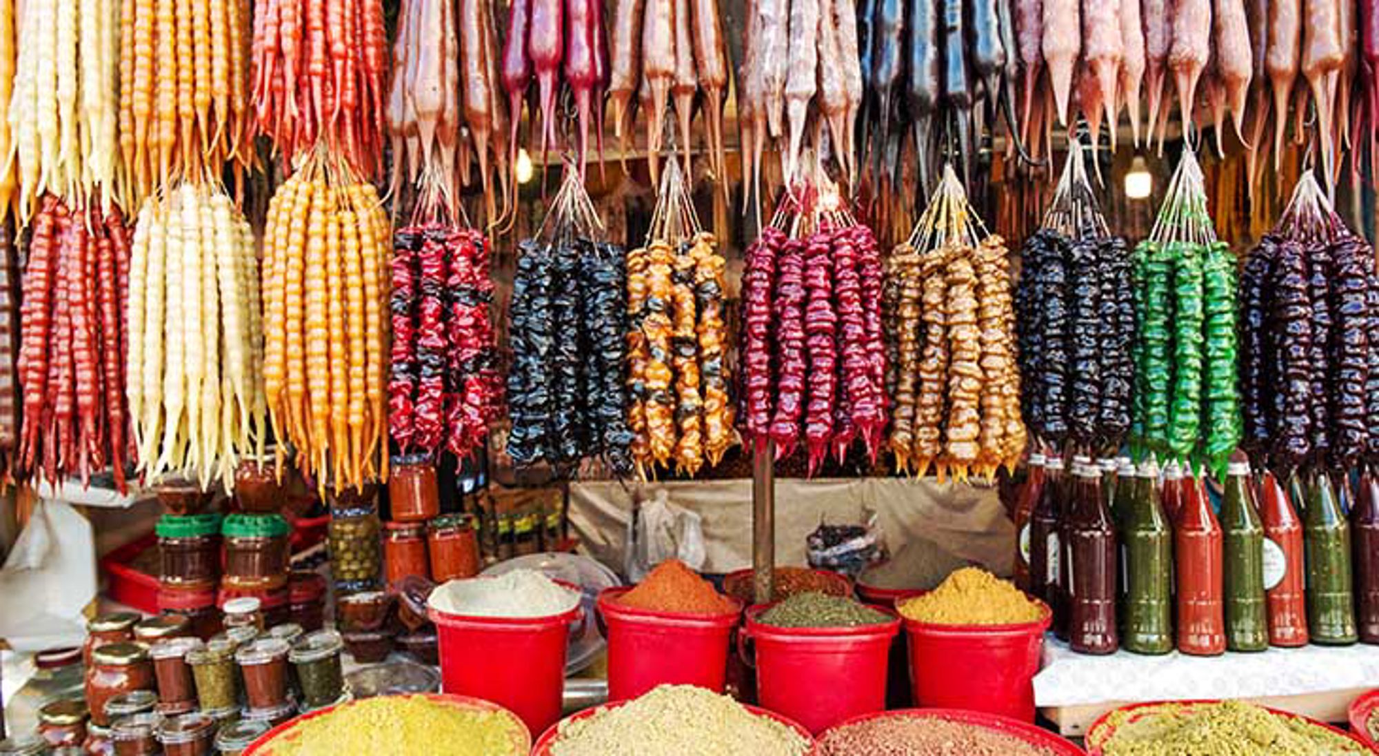 Georgische keuken Kleurrijke marktstalletje met hangende gedroogde producten, kruiden in rode bakken en flessen siroop.
