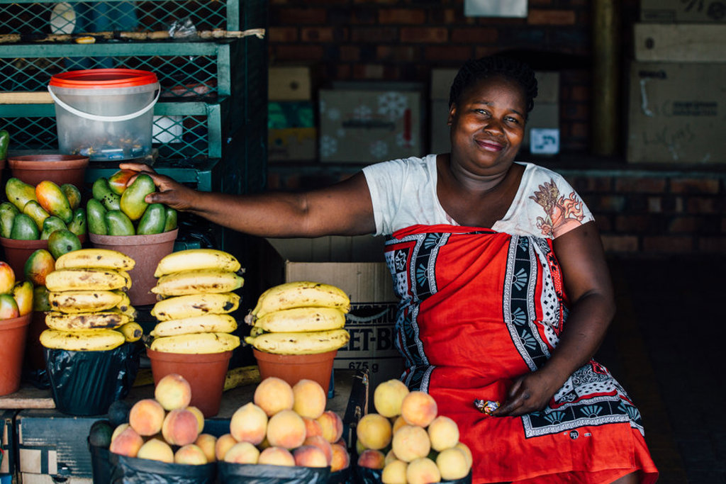 Marktvrouw bij een fruitkraam met mango’s, bananen en perziken tijdens een groepsrondreis door Zuid-Afrika, eSwatini en Lesotho.