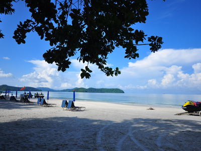 Rustig zandstrand op Langkawi met ligbedden, parasols en uitzicht op zee en groene eilanden, Maleisië.