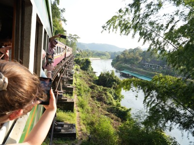 Passagiers maken foto’s vanuit de trein op de brug over de River Kwai bij Kanchanaburi, Thailand.