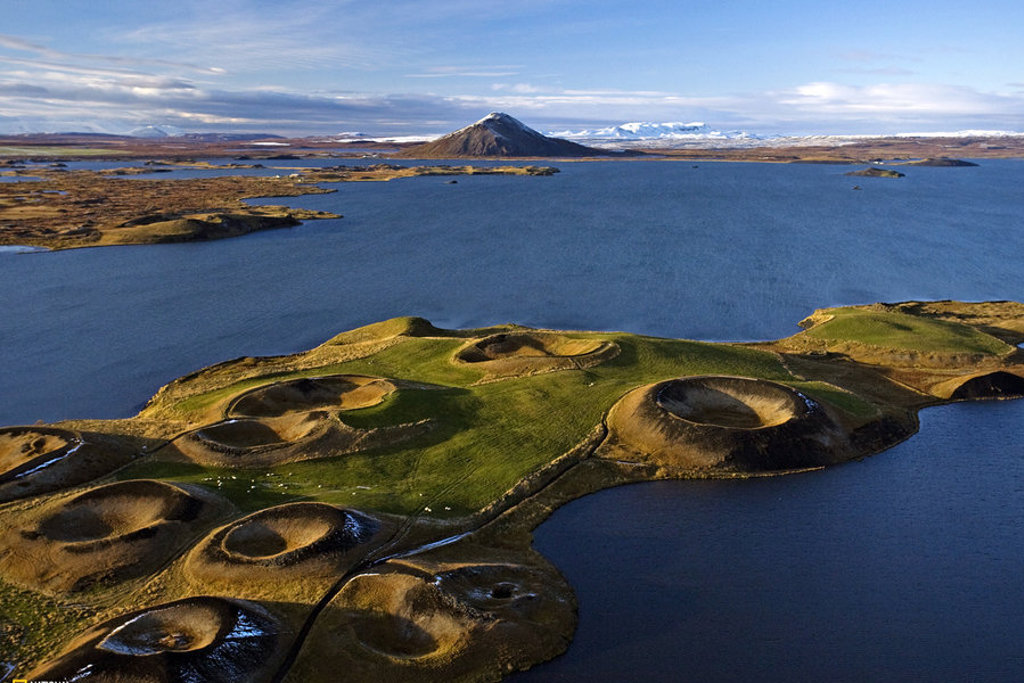 Groene pseudokraters bij het Myvatnmeer in IJsland, met vulkanisch landschap en besneeuwde bergen op de achtergrond.