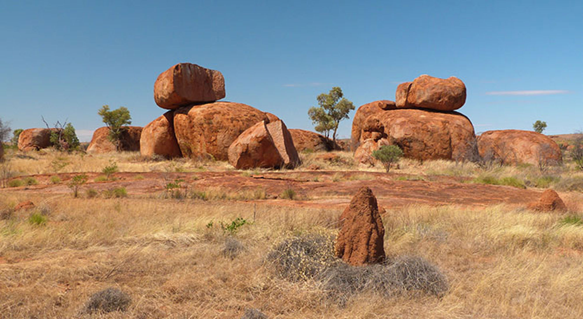 Rode rotsformaties en grasland in de outback onder een helderblauwe lucht.