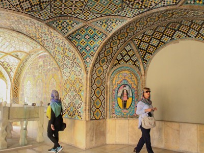 Bezoekers onder mozaïekbogen met kleurrijke tegelpatronen in een Iraans paleisinterieur.