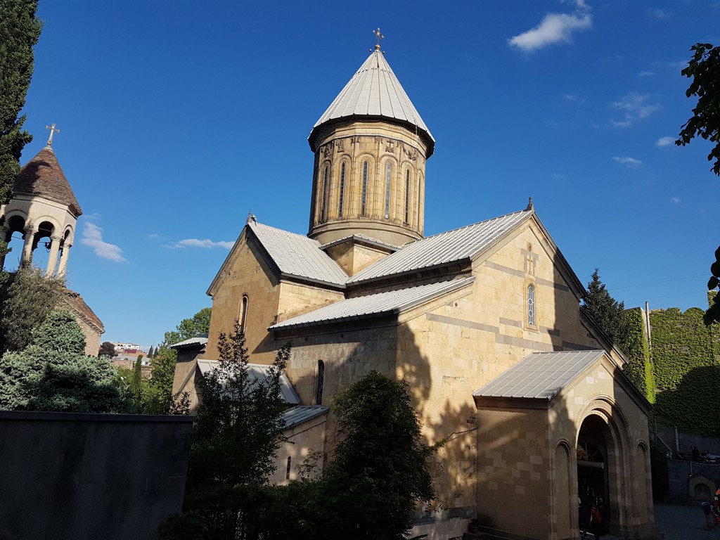 Georgisch-orthodoxe kerk in Tbilisi, Georgië, met koepel en klokkentoren onder een blauwe lucht.
