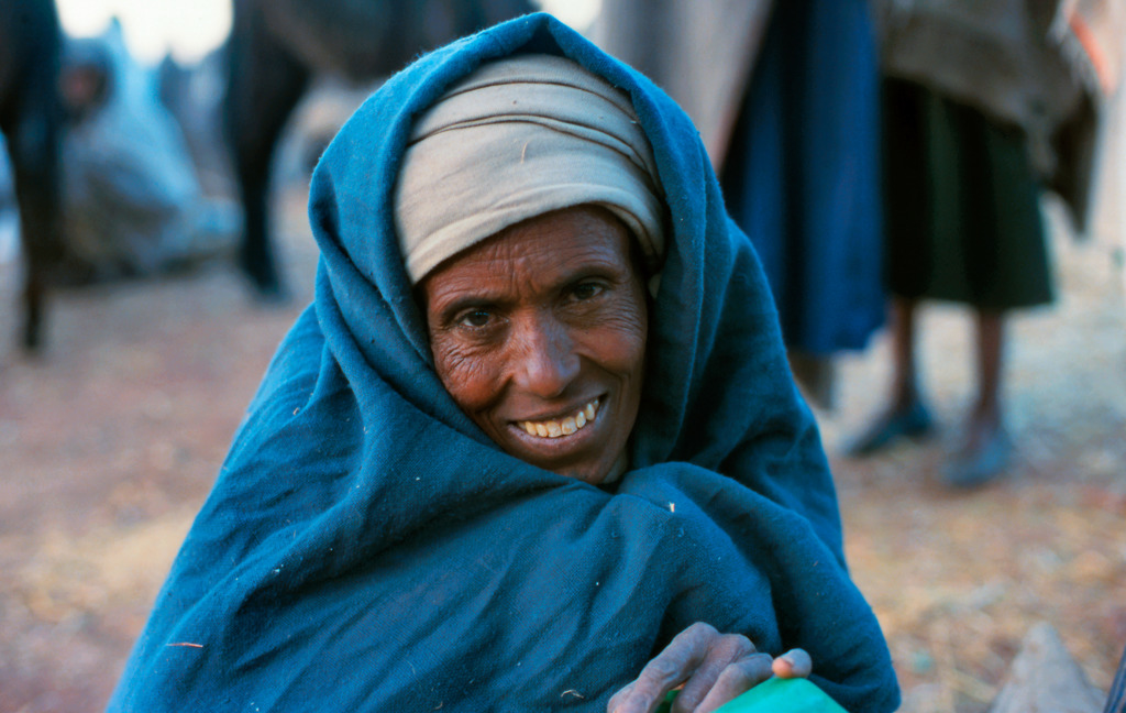 Portret van een glimlachende Ethiopische vrouw met blauwe omslagdoek, tijdens een groepsrondreis door Ethiopië.
