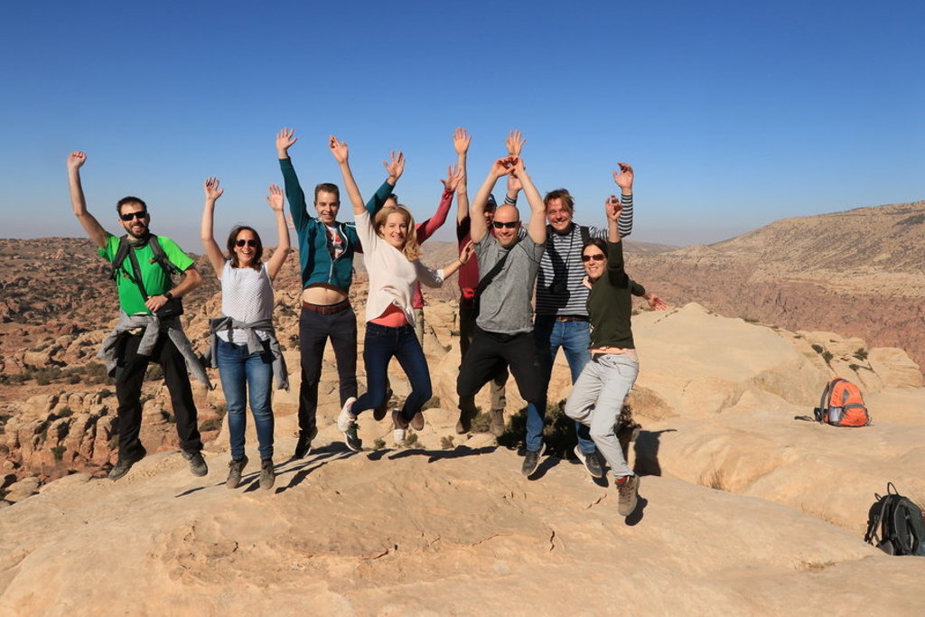 Groepsrondreis Jordanië: reizigers springen juichend op rotsen met uitzicht over het woestijnlandschap.