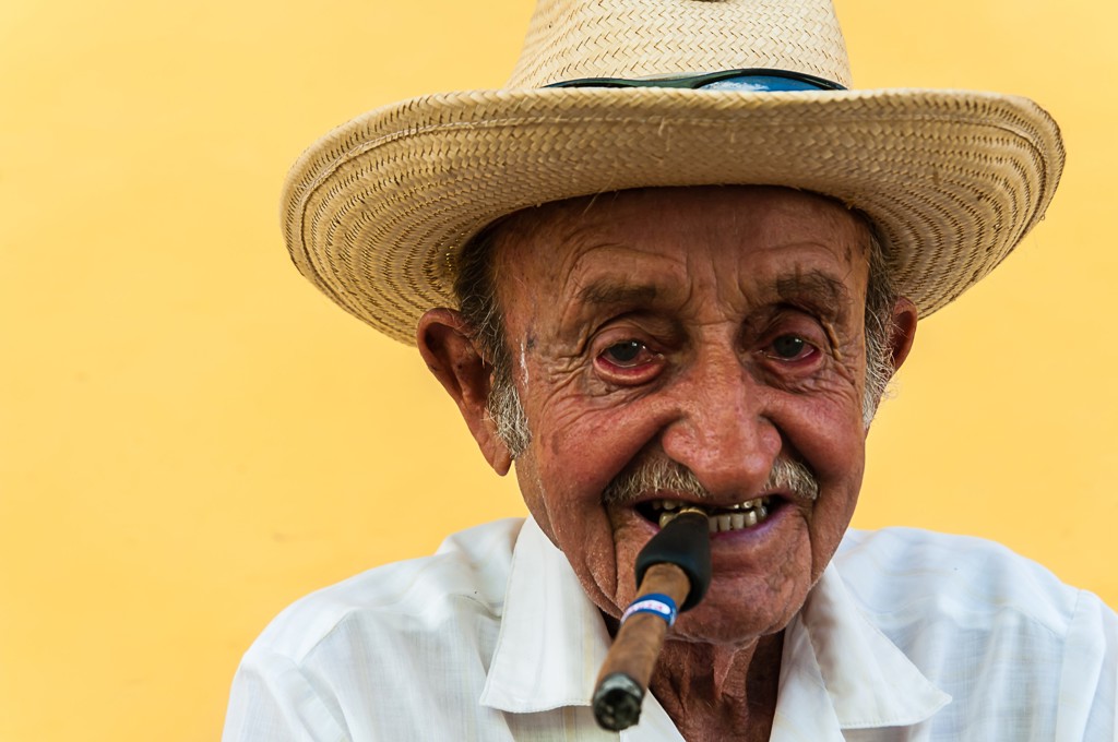 Cubaanse man met strohoed en sigaar, portret tegen gele achtergrond.