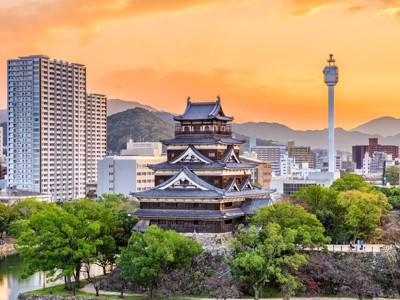 Hiroshima Castle bij zonsondergang, omringd door stadsgebouwen en groene bomen in Japan.