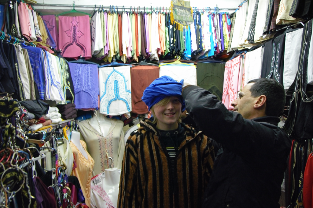 Jongen past een blauwe tulband in een kledingwinkel op een markt in Marokko tijdens een familiereis.