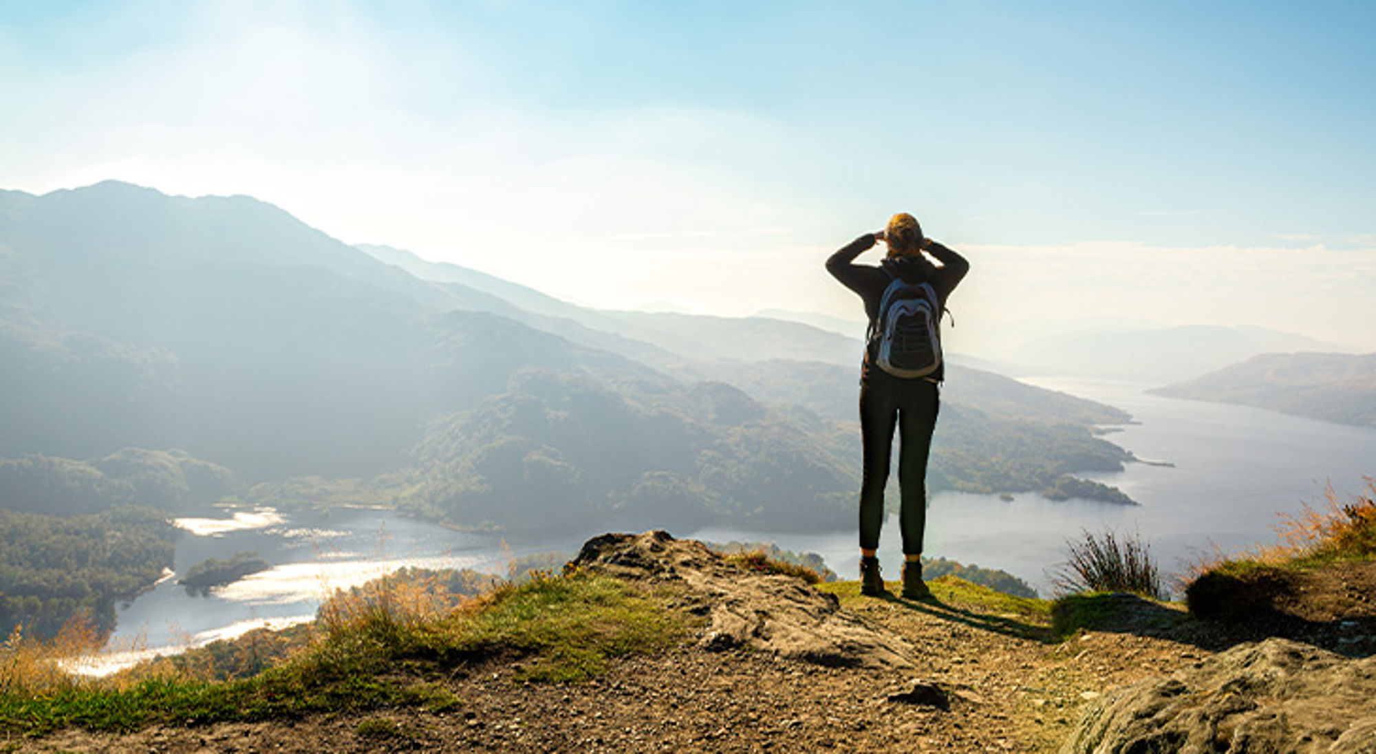 Wandelen in Schotland Wandelaar met rugzak kijkt uit over bergen en een meer vanaf een uitzichtpunt.