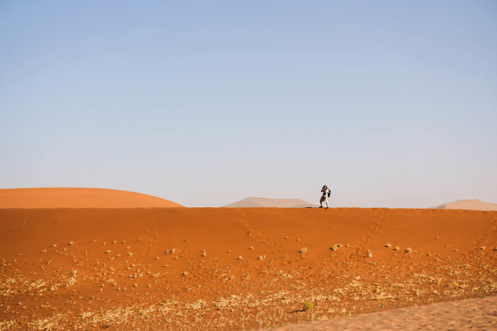 Reiziger loopt over een rode zandduin in Namibië tijdens groepsrondreis Zuidelijk Afrika (kampeerreis).