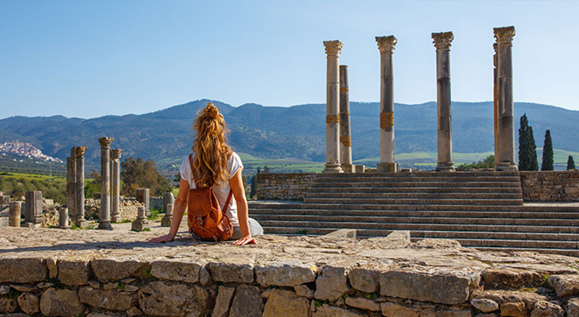 Volubilis Toerist bij de Romeinse ruïnes van Volubilis in Marokko, met zuilen en bergen op de achtergrond.