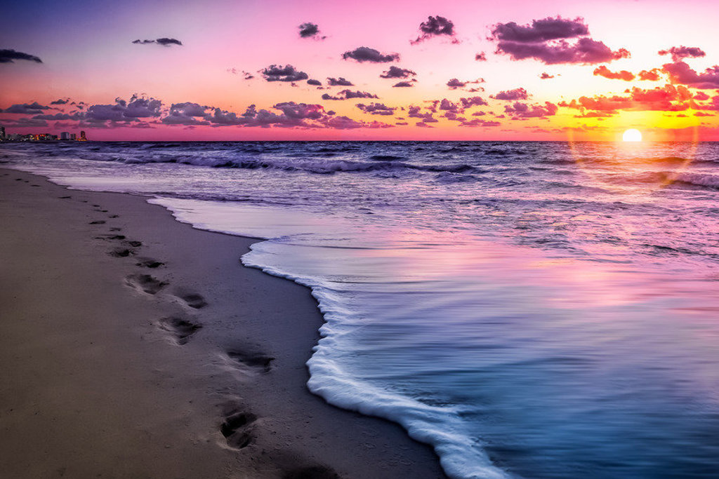 Zonsondergang op een zandstrand met voetstappen langs de branding in Mexico.